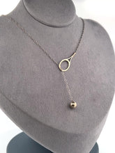 Load and play video in Gallery viewer, The newest design by Adeline - this unusual necklace is a tennis lovers delight.   The solid gold ball threads through the racket and can be worn higher or lower on the neck.  This piece was hand made in the jewelry district of Los Angeles by a fine jewel craft team.  The racket is 1&quot; long and the ball is 6mm around.  Light yet strong enough to play (and win) in.
