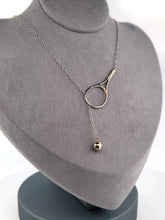 Load and play video in Gallery viewer, The newest design by Adeline - this unusual necklace is a tennis lovers delight.   The solid gold ball threads through the racket and can be worn higher or lower on the neck.  This piece was hand made in the jewelry district of Los Angeles by a fine jewel craft team.  The racket is 1.5&quot; long and the ball is 6mm around.  Light yet strong enough to play (and win) in.
